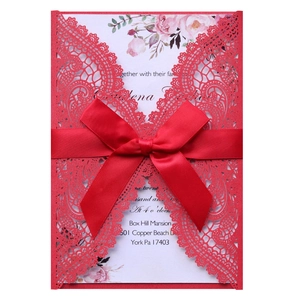 Detail of red laser-cut wedding invitation with intricate lace pattern and satin ribbon