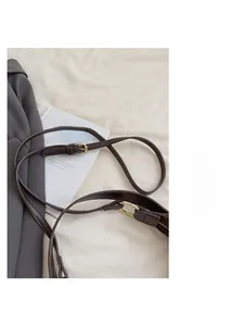 Detail of dark brown leather shoulder strap with gold buckle on a minimalist bag