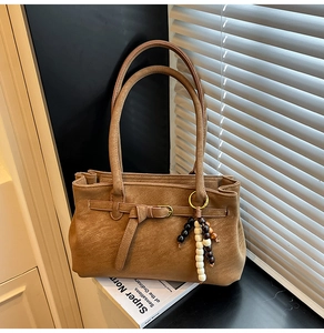 Detail of matte tan bucket bag with gold buckle and tri-color beaded pendant charm