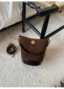 Detail of vintage brown suede bucket bag featuring a gold fashion logo and metal hardware