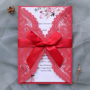 Detailed laser-cut red lace wedding invitation with an elegant satin bow and floral insert