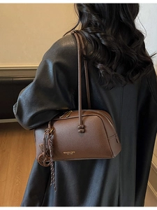 Sac bowling chic en cuir marron foncé avec logo doré et accessoire de charme tressé