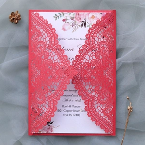 Detail of red laser-cut hollow lace wedding invitation with floral insert and pinecones