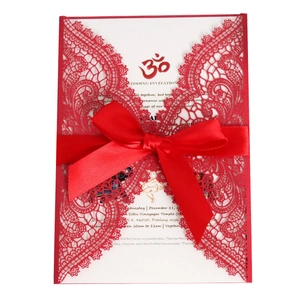 Detail of red laser cut wedding invitation with white insert and decorative silk ribbon