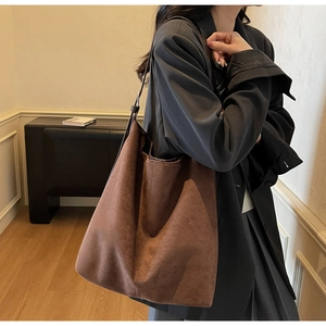 Detailed view of the large brown suede bucket bag worn by a model in a minimal interior