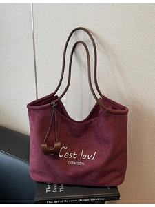 Burgundy suede tote bag with letter embroidery and brown straps on art books