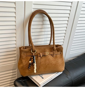 Detail of camel bucket bag featuring retro beaded tassel charm on white books