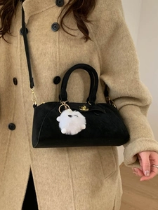 Borsa a mano nera con ciondolo di peluche e chiusura dorata su un cappotto beige