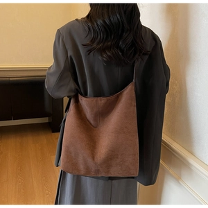 Detailed view of large vintage brown suede bucket bag worn by model in cozy indoor setting