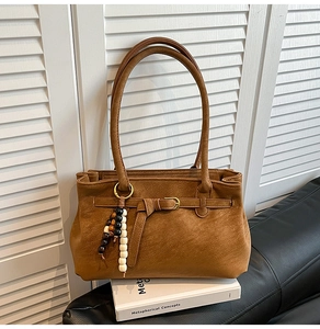 Detail of caramel brown bucket bag featuring wood bead charm and stylish strap buckle