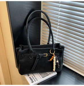 Detail of black matte bucket bag with golden metal buckle and wooden bead decorative pendant