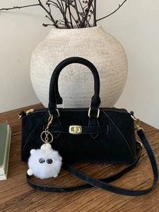 Borsa a mano nera minimalista con chiusura dorata e ciondolo di peluche su legno