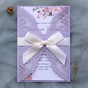 Detail of laser-cut purple lace wedding invitation with white ribbon and floral insert