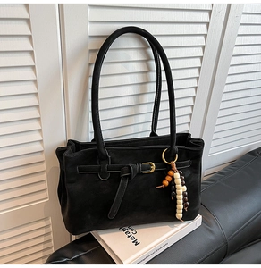 Detail of a black suede bucket bag featuring long straps and ethnic beaded tassel charm