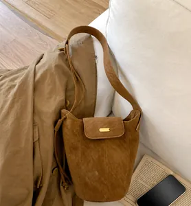 Detail of brown suede bucket bag with gold metal buckle on a white sofa setting