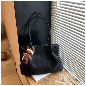 Detail shot of a black slouchy tote bag with a brown knit bear charm on a wooden surface