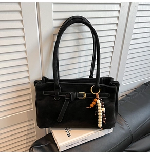 Detail of black suede bucket bag featuring buckle strap and beaded tassel pendant