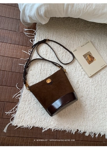 Detailed macro view of dark brown suede bucket bag with gold circular metal buckle ornament