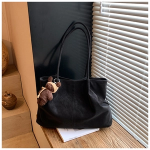 Detail of black matte tote bag with brown bear charm and soft decorative stitching