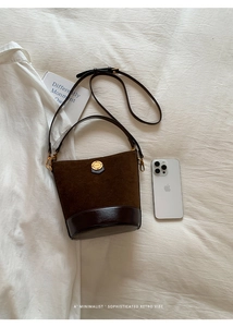 Detail of vintage brown suede bucket bag with gold logo emblem and dual strap design