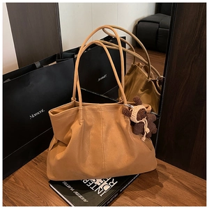 Detail of camel tote bag with matte texture, pleats, and cute bear charm in warm studio setting