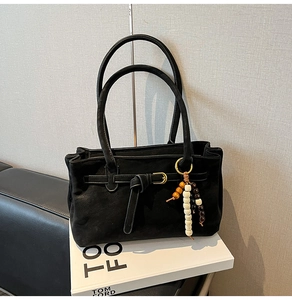 Detail of black suede bucket bag featuring knotted strap buckle and beaded charm accessory