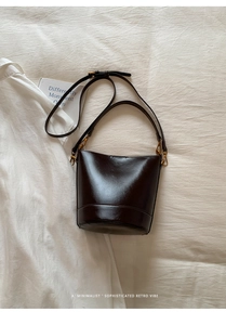 Top view of dark brown faux leather bucket bag with golden hardware on white fabric