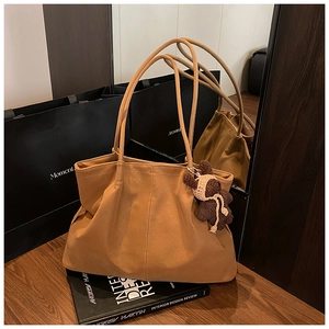 Detail of caramel suede tote bag with a cute teddy bear charm on a wooden surface