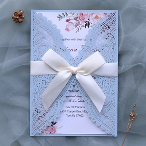 Close-up of light blue laser cut lace wedding invitation with a white ribbon and floral card
