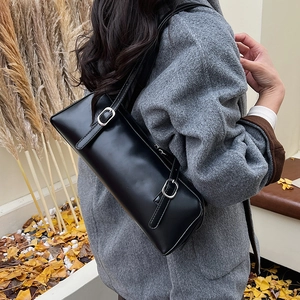 Detail of minimalist black matte leather underarm bag with silver buckles on autumn background
