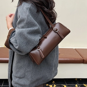 Detail of dark brown cylindrical shoulder bag with silver buckles in an autumn setting