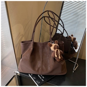 Brown leather tote bag featuring a cute knitted bear charm and minimalist stitch detail