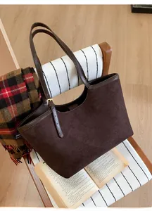Détail du sac cabas en daim marron foncé avec anses en cuir et boucles dorées sur une chaise