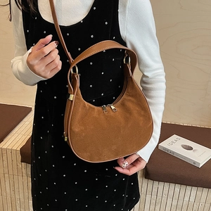 Detail of a brown suede crescent bag featuring double gold zippers and leather handle