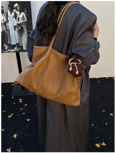 Detail view of large brown pleated tote bag with a small knitted bear charm for fall