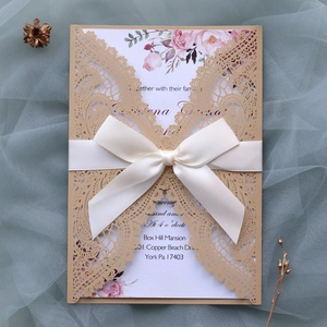 Detailed view of laser-cut gold wedding invitation with ribbon and floral insert