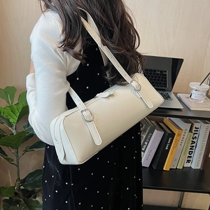 Detail of a creamy white cylindrical shoulder bag with adjustable silver buckle strap