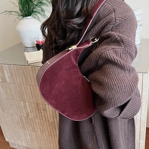 Detail of burgundy suede shoulder bag with gold hardware worn in an elegant interior setting