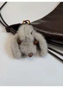 Detail of grey fur rabbit charm with vintage bronze clasp on a brown leather bag