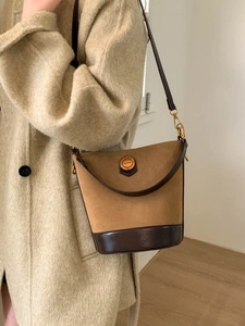 Retro brown suede bucket bag with leather trim worn with a beige wool coat in a warm interior