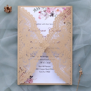 Close-up of laser-cut gold lace wedding invitation with floral inner card and elegant text