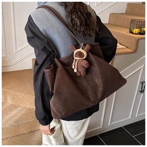 Detail of a brown suede tote bag featuring contrast stitching and a plush bear charm