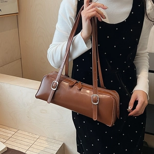 Detail view of brown leather cylinder shoulder bag with dual silver buckle straps