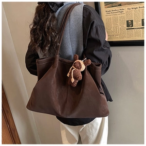 Detail of a large dark brown matte leather tote bag featuring a cute knit bear pendant