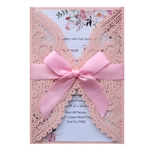 Detail of pink laser cut wedding invitation with lace pattern and elegant satin ribbon bow