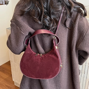 Detail of dark red suede crescent shoulder bag with adjustable strap on a model