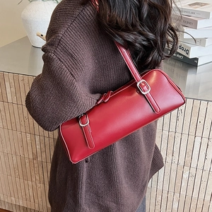 Detail view of burgundy cylindrical shoulder bag with silver buckles and leather texture