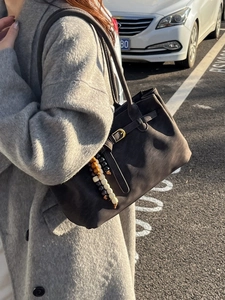 Retro brown suede bucket bag with metal buckle and beaded charm worn by model