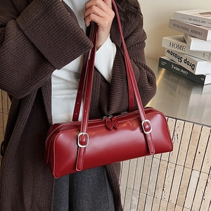 Close-up of a red cylindrical shoulder bag with silver buckles and a smooth glossy finish