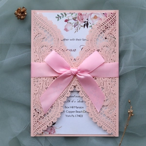 Close-up of laser-cut pink wedding invitation with satin ribbon and floral inner card